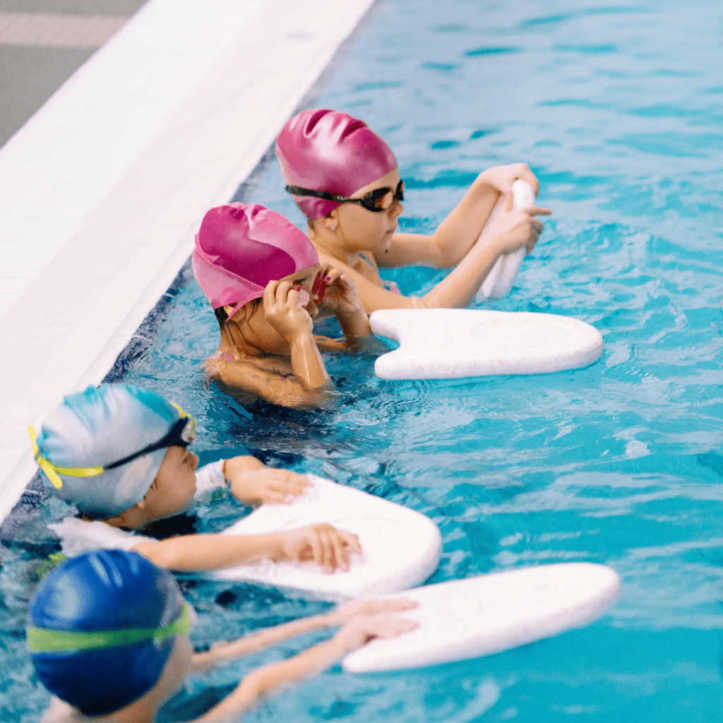 Groupe d'enfants dans l'eau, participant à un cours de natation collectif encadré par un professionnel, dans un environnement sécurisé et convivial.